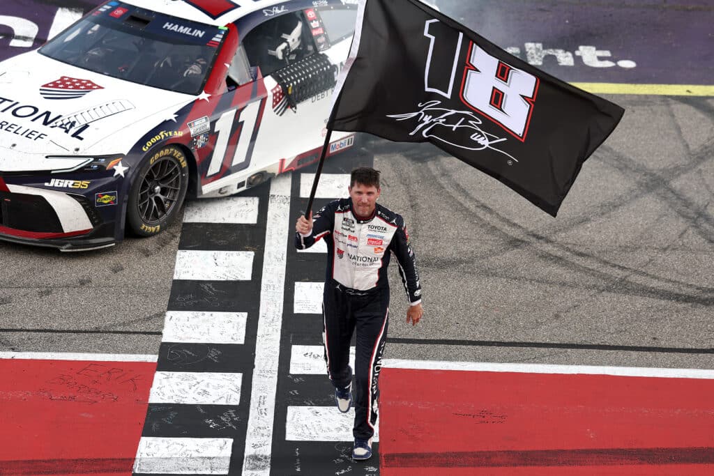 Denny Hamlin celebrates with a Kyle Busch flag after winning at Michigan.
