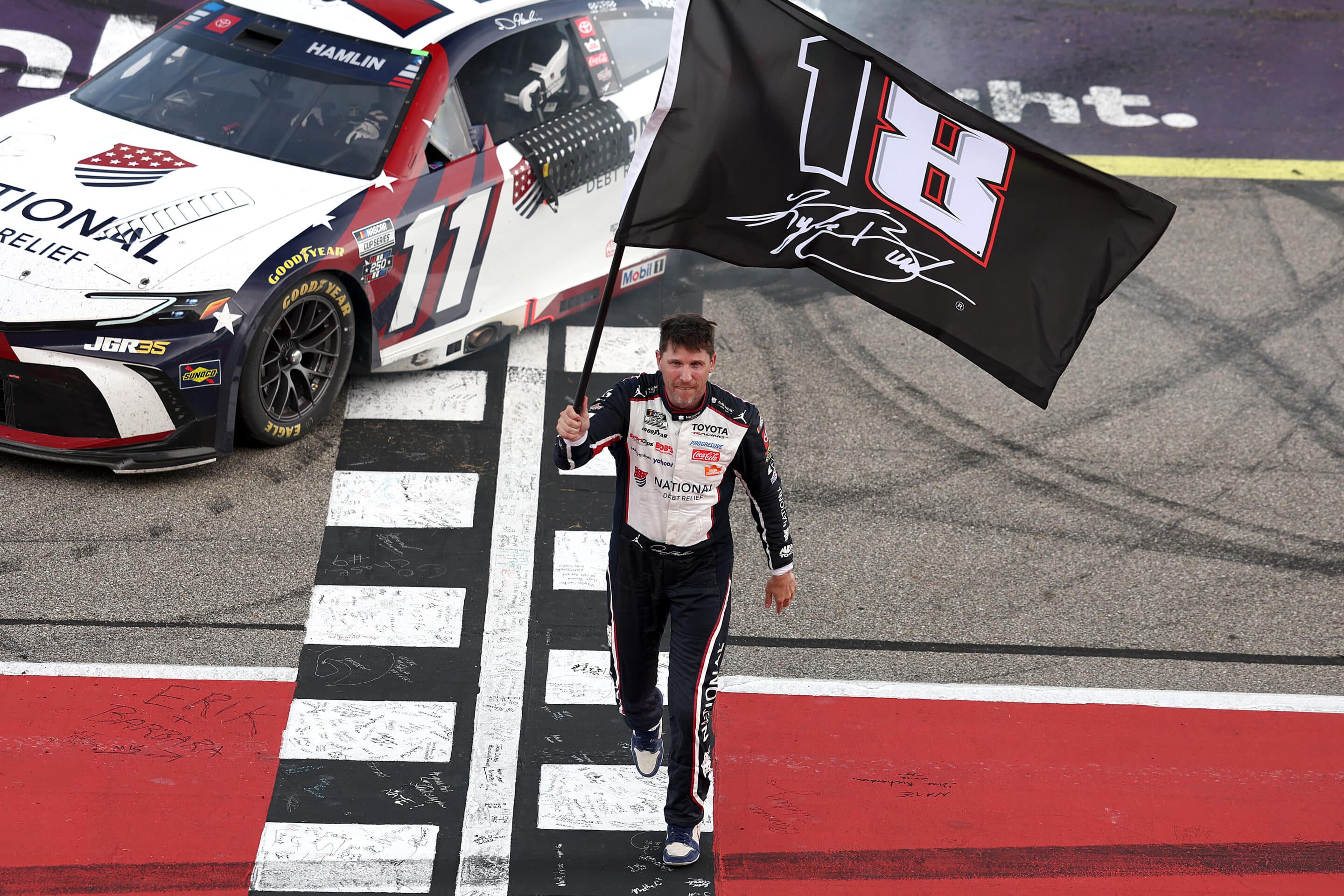 Denny Hamlin celebrates with a Kyle Busch flag after winning at Michigan.
